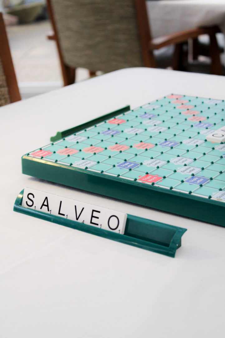 A Scrabble board is on a table, and a tile rack displays the letters S, A, L, V, E and O.