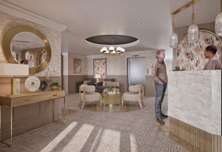A man speaks with a receptionist at a modern, well-lit hotel reception. The lobby features elegant furniture, artwork, and a large round mirror.